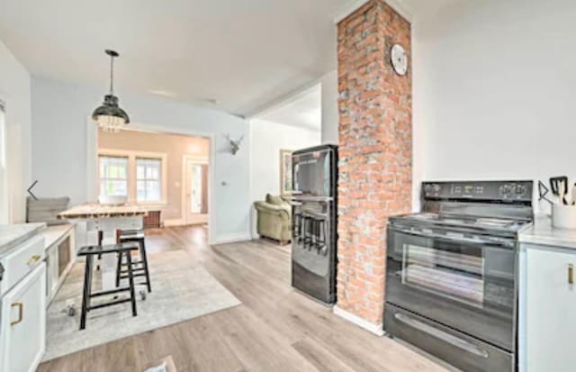 kitchen with pendant lighting, white cabinetry, black electric range, and light hardwood / wood-style floors