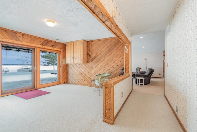 hall with light carpet, a textured ceiling, and wood walls