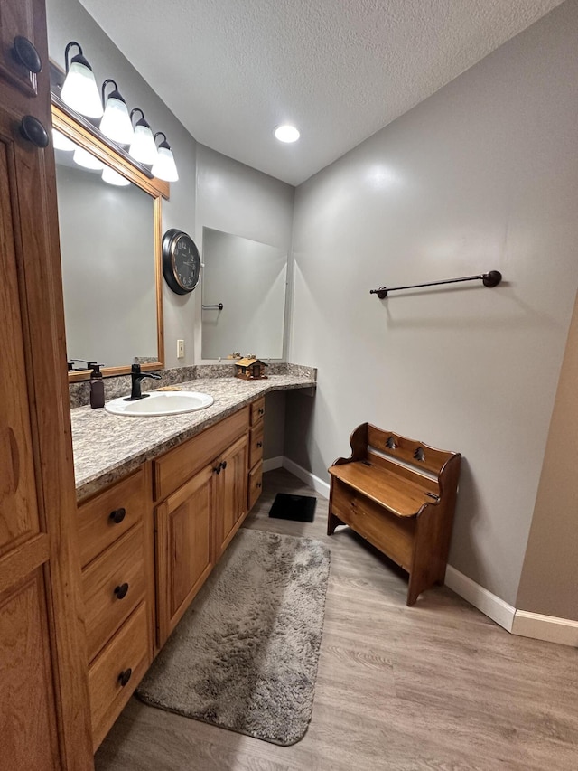 bathroom with a textured ceiling, baseboards, wood finished floors, and vanity