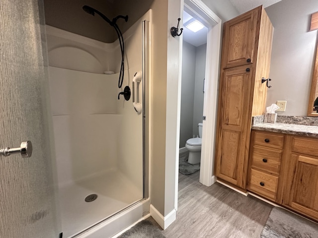 bathroom featuring toilet, wood finished floors, vanity, baseboards, and a shower stall