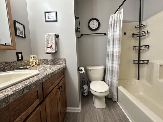 bathroom featuring baseboards, toilet, wood finished floors, shower / bath combination with curtain, and vanity