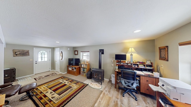 office area with light wood-type flooring, a wood stove, baseboards, and a textured ceiling