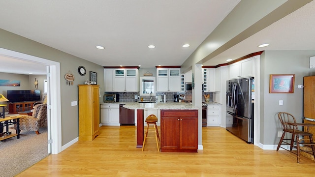 kitchen featuring backsplash, appliances with stainless steel finishes, glass insert cabinets, a kitchen island, and a kitchen bar