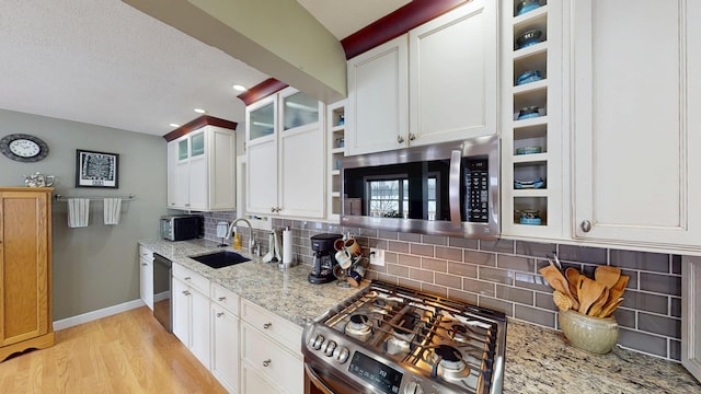 kitchen featuring baseboards, light wood-style flooring, light stone countertops, stainless steel appliances, and a sink