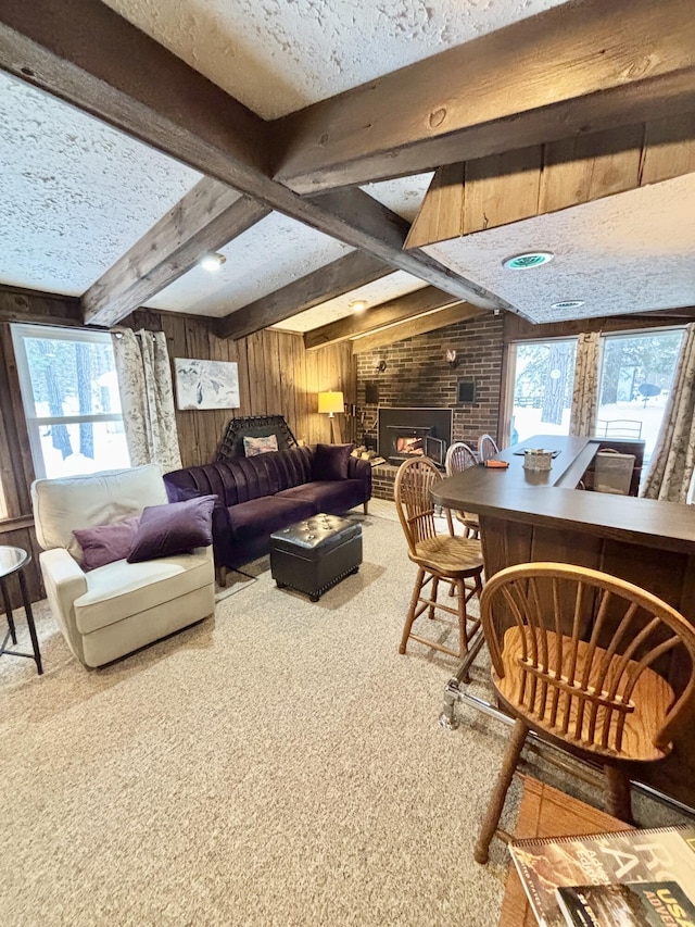 living room with wood walls, a textured ceiling, a brick fireplace, carpet flooring, and beamed ceiling