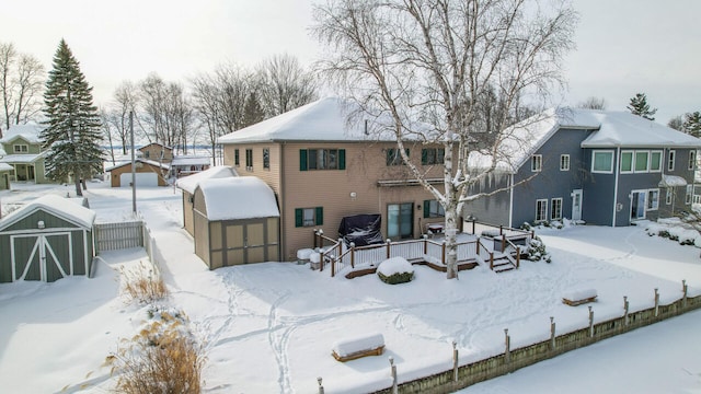 snow covered rear of property with a shed, a deck, and an outdoor structure