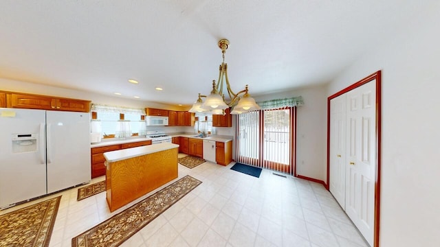 kitchen with pendant lighting, light countertops, brown cabinetry, a sink, and white appliances