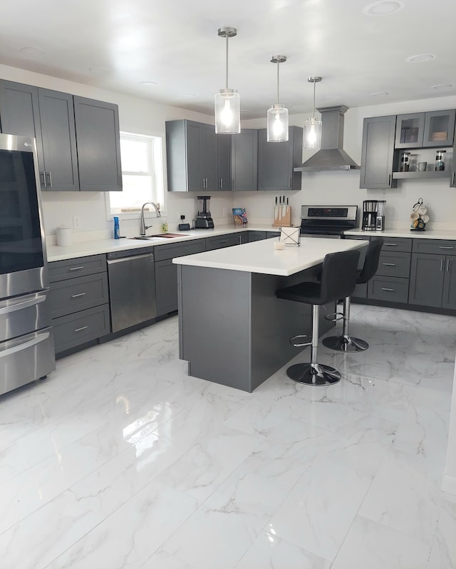 kitchen featuring a kitchen island, appliances with stainless steel finishes, decorative light fixtures, sink, and wall chimney range hood