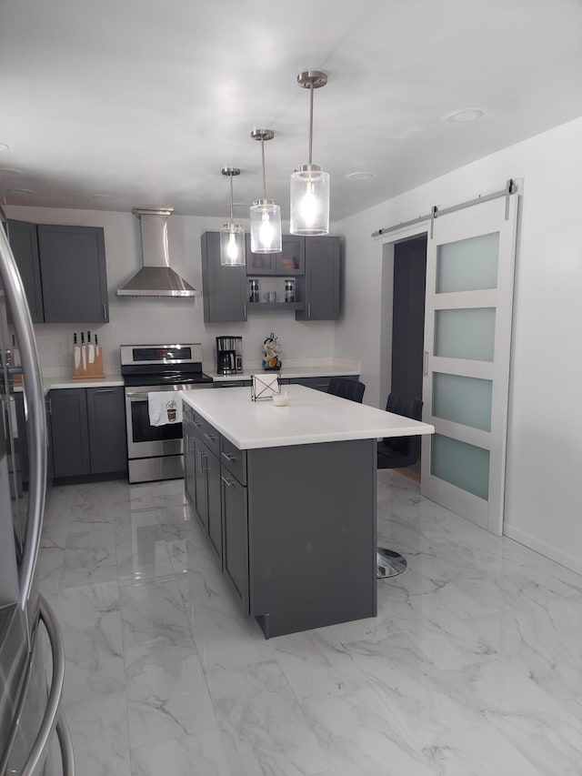 kitchen featuring wall chimney range hood, stainless steel appliances, a kitchen island, decorative light fixtures, and a barn door