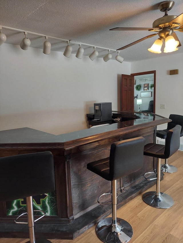 bar with hardwood / wood-style flooring, ceiling fan, and a textured ceiling