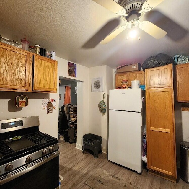 kitchen with stainless steel gas range oven, ceiling fan, wood finished floors, freestanding refrigerator, and a textured ceiling