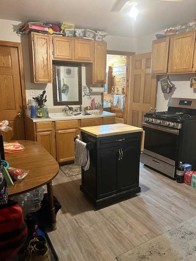 kitchen featuring light wood-style flooring, a kitchen island, a ceiling fan, light countertops, and stainless steel range with gas cooktop