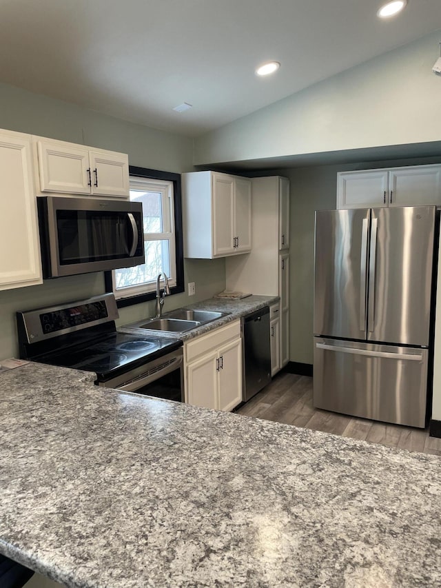 kitchen with appliances with stainless steel finishes, sink, vaulted ceiling, and white cabinets