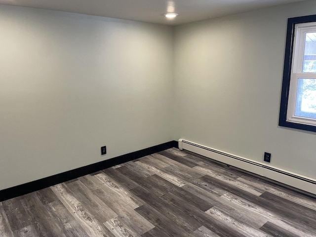 unfurnished room featuring a baseboard heating unit and dark hardwood / wood-style flooring