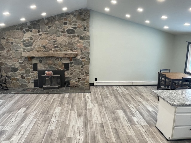 interior space featuring lofted ceiling, light hardwood / wood-style flooring, a wood stove, and baseboard heating