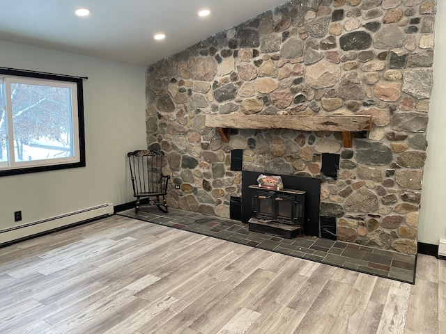 unfurnished living room with a wood stove, wood-type flooring, and a baseboard radiator