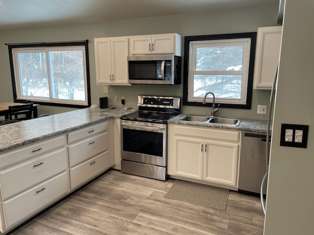 kitchen with white cabinets, light wood-type flooring, appliances with stainless steel finishes, and sink