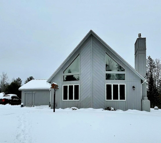 snow covered house with a garage and a chimney