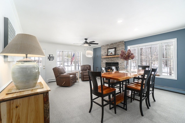 carpeted dining space with ceiling fan, a stone fireplace, baseboard heating, and crown molding