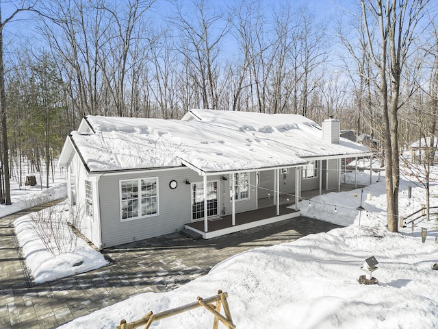 snow covered back of property with a chimney and a porch