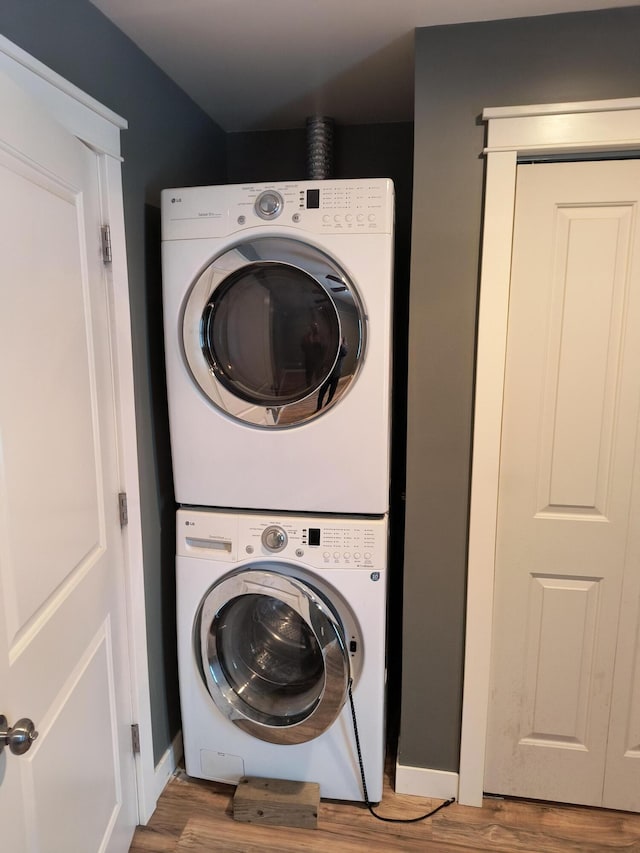 laundry area with baseboards, laundry area, wood finished floors, and stacked washer / drying machine