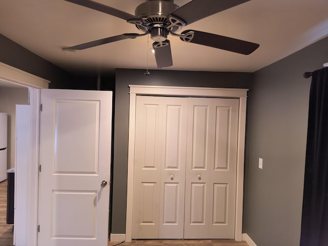 unfurnished bedroom with freestanding refrigerator, a closet, a ceiling fan, and baseboards