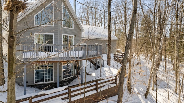 snow covered back of property with a deck and a chimney