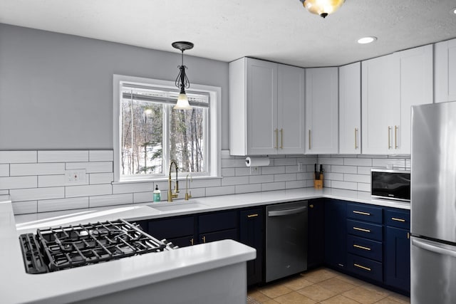 kitchen with a sink, white cabinetry, light countertops, appliances with stainless steel finishes, and blue cabinetry