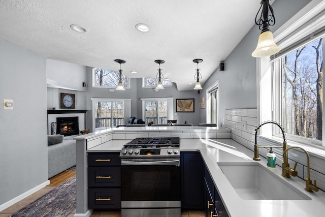 kitchen featuring light countertops, gas stove, open floor plan, a sink, and a peninsula