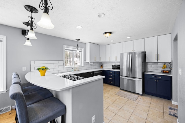 kitchen featuring white cabinets, freestanding refrigerator, blue cabinets, a peninsula, and light countertops