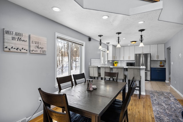 dining room with recessed lighting, a textured ceiling, baseboards, and light wood finished floors