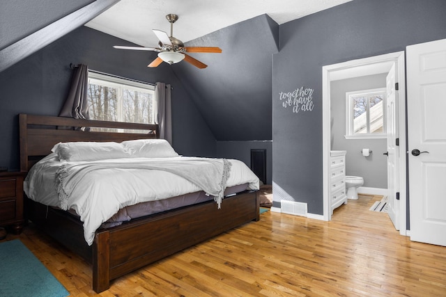 bedroom featuring visible vents, baseboards, ensuite bathroom, vaulted ceiling, and light wood-type flooring