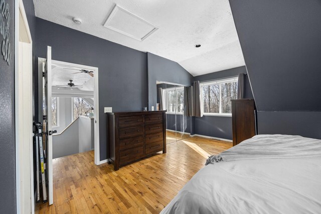 bedroom with lofted ceiling, a textured ceiling, baseboards, light wood-type flooring, and attic access