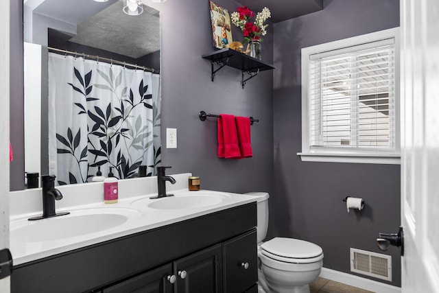 full bathroom featuring toilet, double vanity, a sink, and visible vents