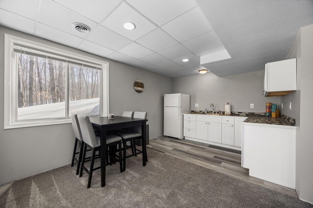 kitchen featuring dark countertops, visible vents, freestanding refrigerator, white cabinets, and a sink