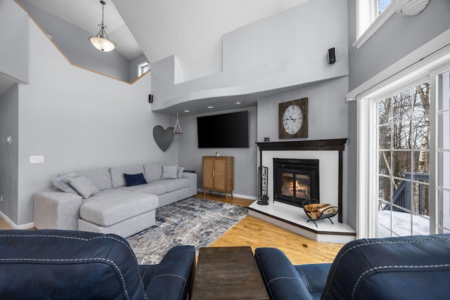 living area with high vaulted ceiling, wood finished floors, a tile fireplace, and a healthy amount of sunlight