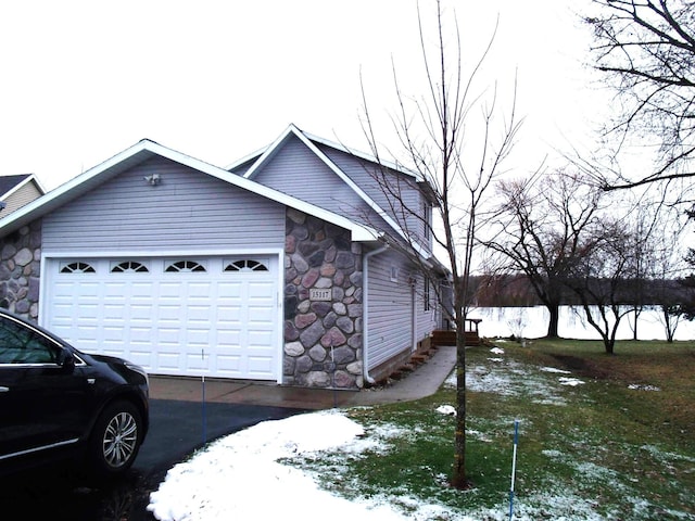 view of snow covered exterior featuring an attached garage, stone siding, and driveway