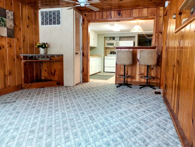 kitchen featuring wooden walls, light colored carpet, white microwave, ceiling fan, and stove