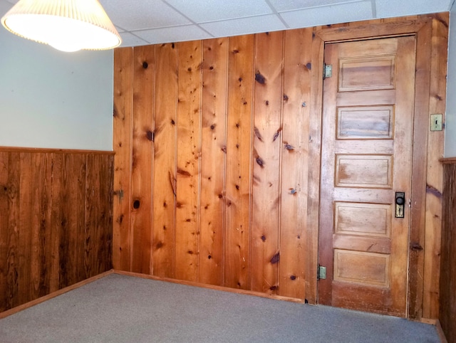 carpeted empty room with a drop ceiling and wood walls