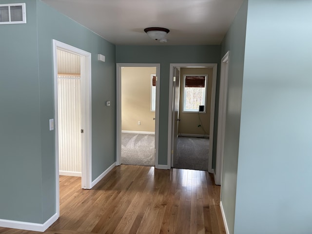 hall with visible vents, baseboards, and wood finished floors