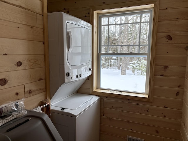 clothes washing area featuring stacked washer and dryer, visible vents, laundry area, and wood walls