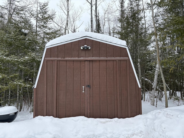 snow covered structure featuring an outdoor structure and a storage shed