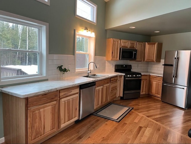 kitchen with light stone countertops, a sink, light wood-style floors, appliances with stainless steel finishes, and decorative backsplash