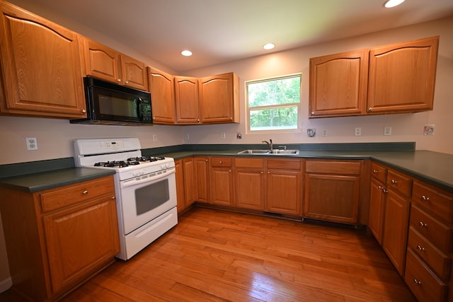 kitchen featuring light wood finished floors, white gas range, dark countertops, a sink, and black microwave