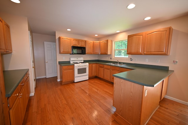 kitchen with dark countertops, white gas range, light wood-style floors, black microwave, and a sink