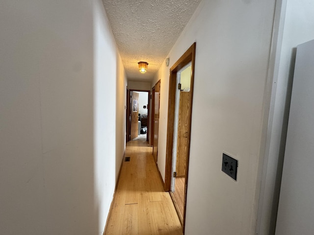 hall featuring a textured ceiling, light wood finished floors, and visible vents