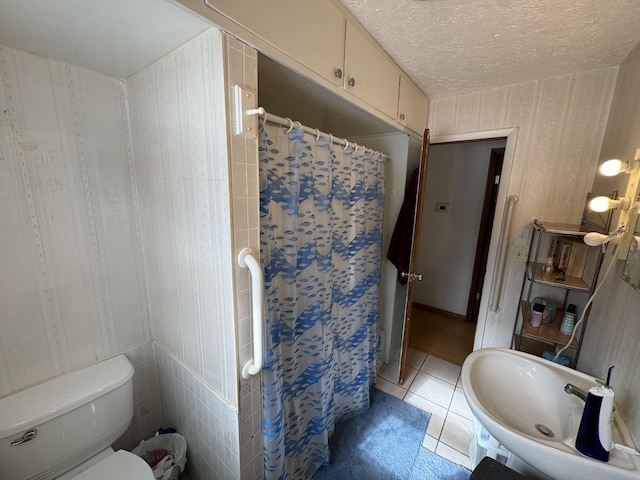 full bathroom featuring a textured ceiling, curtained shower, tile patterned flooring, toilet, and a sink