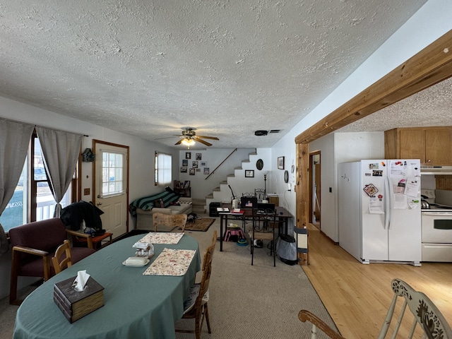 dining space featuring a textured ceiling, stairway, a ceiling fan, and light wood-style floors