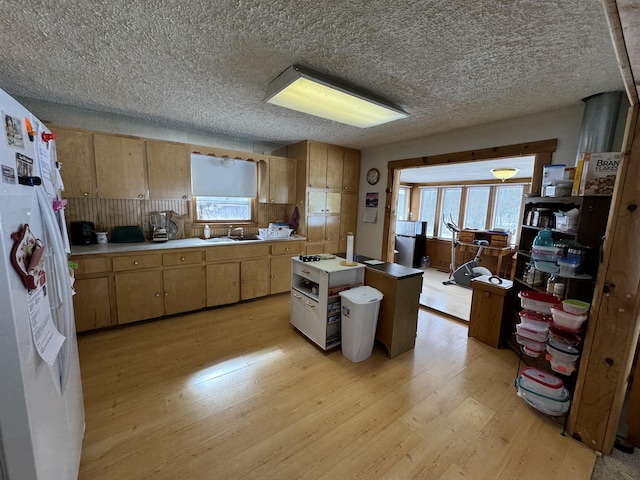 kitchen with light countertops, light wood-style floors, freestanding refrigerator, a kitchen island, and a sink