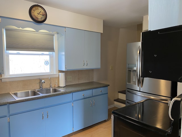 kitchen with dark countertops, stainless steel fridge, a sink, and blue cabinetry